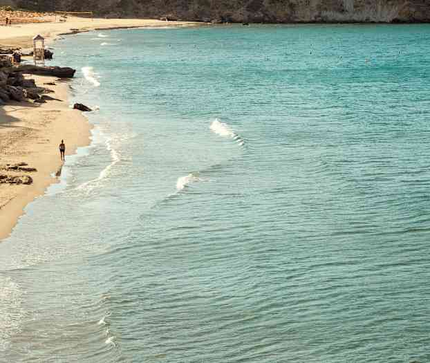 Strand med klart vatten och en person som går längs strandkanten. (AI-genererad text)