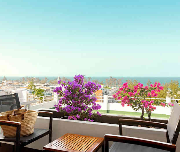 En balkong med bord och stolar, blommor och havsutsikt. (AI-genererad text)