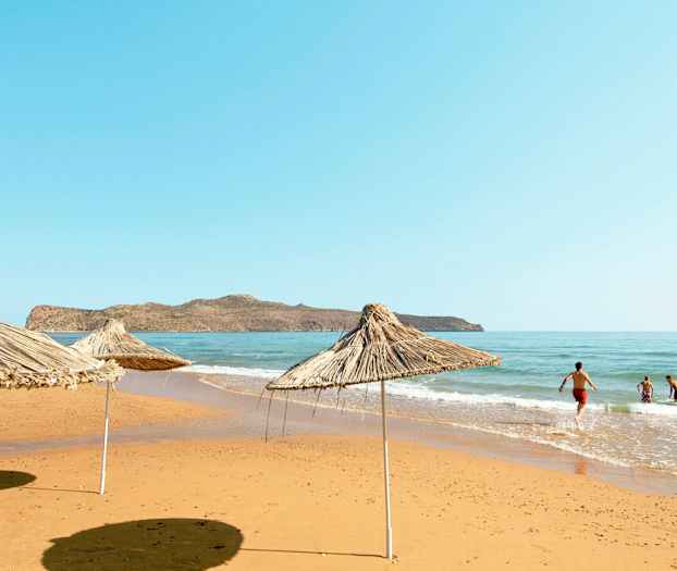 Strand med parasoller av vass samt människor som badar i havet. (AI-genererad text)