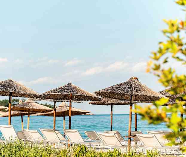 Strand med solstolar och parasoller av halm vid havet. (AI-genererad text)