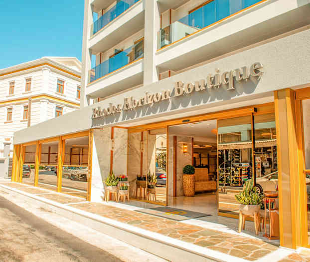 Framsidan av ett hotell med namnet Rhodos Horizon Boutique, med glasdörrar och växter vid ingången. (AI-genererad text)
