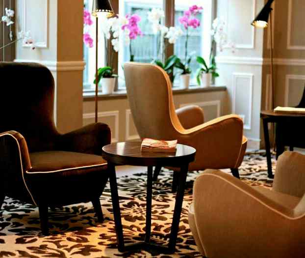 En lounge med bekväma fåtöljer, ett bord och dekorativa blommor i fönstren. (AI-genererad text)