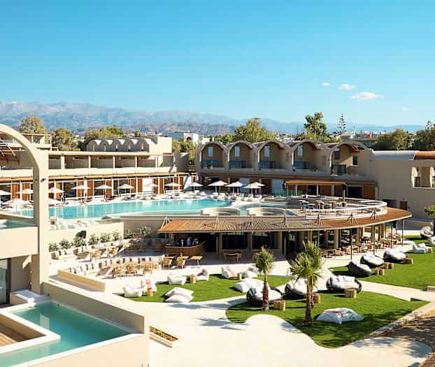 Ett modernt hotell med poolområde och grönskande trädgård, samt berg i bakgrunden. (AI-genererad text)