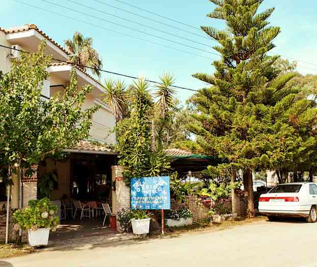 Foto av hotellfasad med träd och en parkerad bil framför. (AI-genererad text)