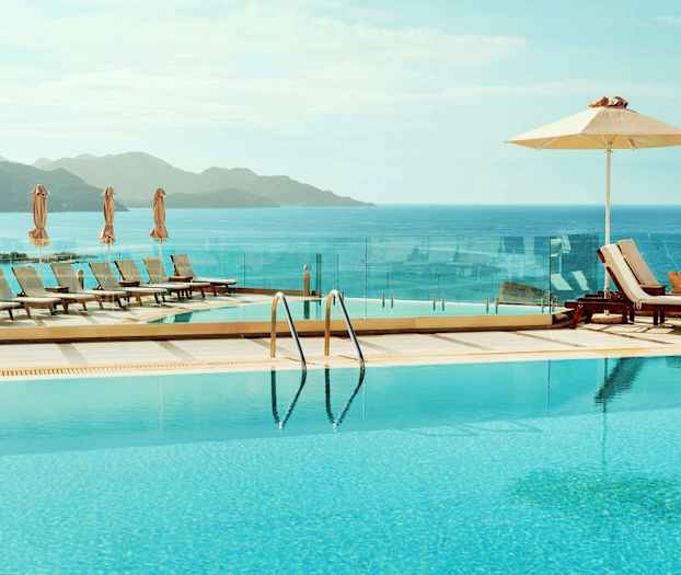 En infinitypool med utsikt över havet och berg, omgiven av solstolar och parasoller. (AI-genererad text)