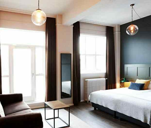 Ett hotellrum med en dubbelsäng, en soffa och ett litet soffbord samt stora fönster med gardiner. (AI-genererad text)