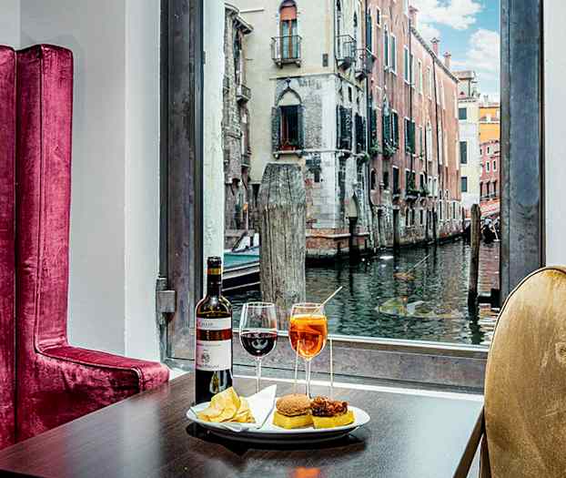 Bord med drycker och tilltugg, bakom syns en kanal med byggnader. (AI-genererad text)