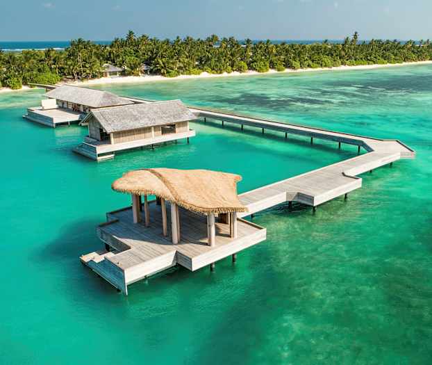 Övervattensbungalower vid en tropisk strand med turkost hav. (AI-genererad text)