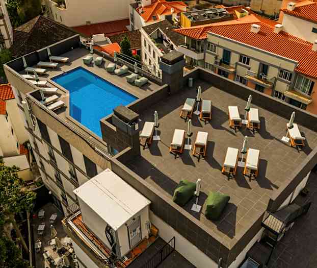 Bild av en takterrass med en blå pool, solstolar och parasoller, omgiven av byggnader med tegeltak. (AI-genererad text)