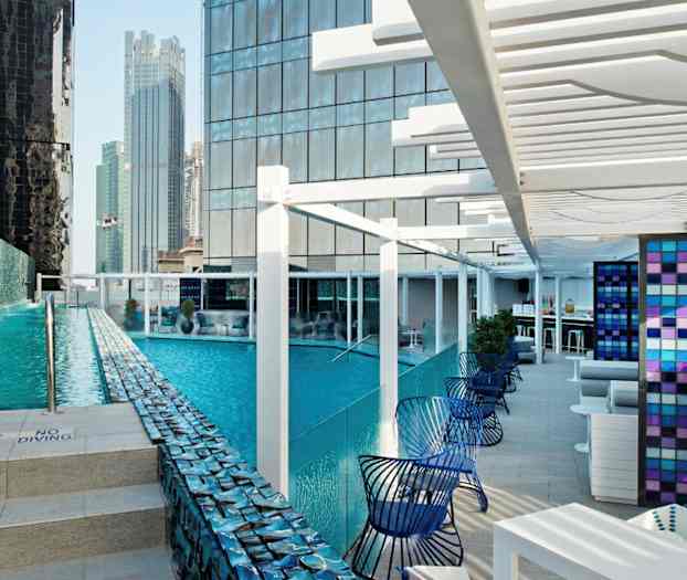 En modern utomhuspool omgiven av höga byggnader med en sittgrupp bredvid. (AI-genererad text)