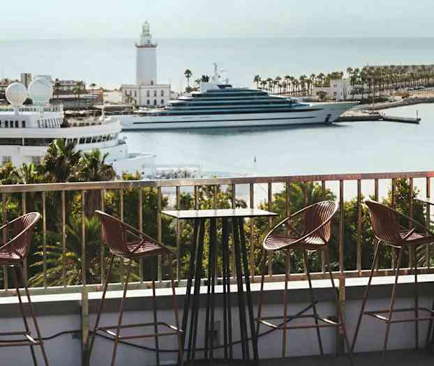 En uteservering med utsikt över en marina med båtar och en fyr. (AI-genererad text)