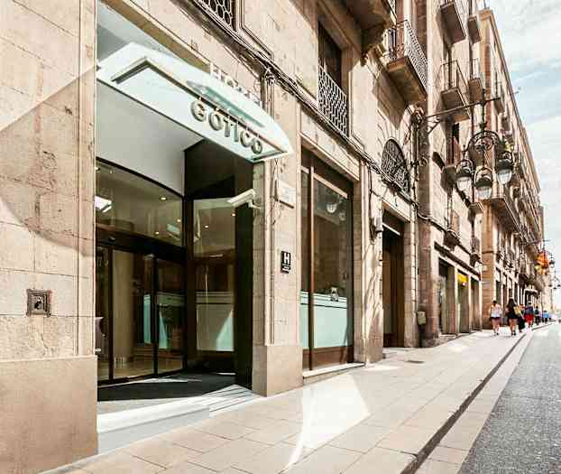 Entrén till en byggnad med glasdörrar, belägen på en gata med byggnader på båda sidor. (AI-genererad text)