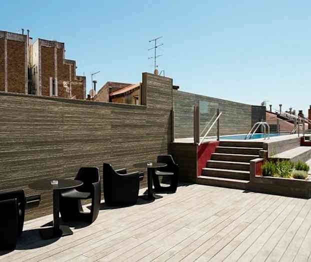 Takterrass med trädeck. Svarta stolar och bord i förgrunden. Trappa leder till en pool. (AI-genererad text)