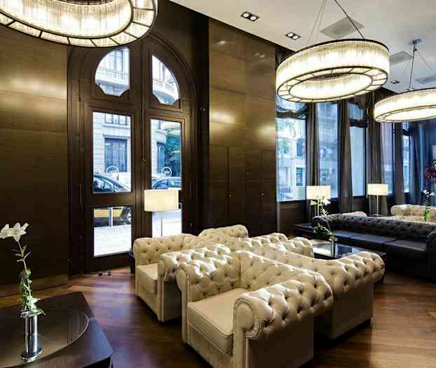 Ett elegant vardagsrum med en sittgrupp i Chesterfield-stil, stora fönster, kristallkronor och trägolv. (AI-genererad text)