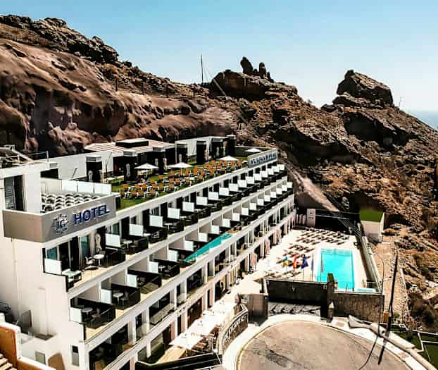 Ett hotell beläget vid en bergssluttning med en poolområde och havsutsikt. (AI-genererad text)