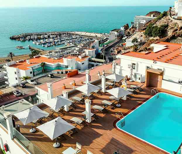 En pool med solstolar och parasoller på en terrass, med utsikt över havet och en marina. (AI-genererad text)