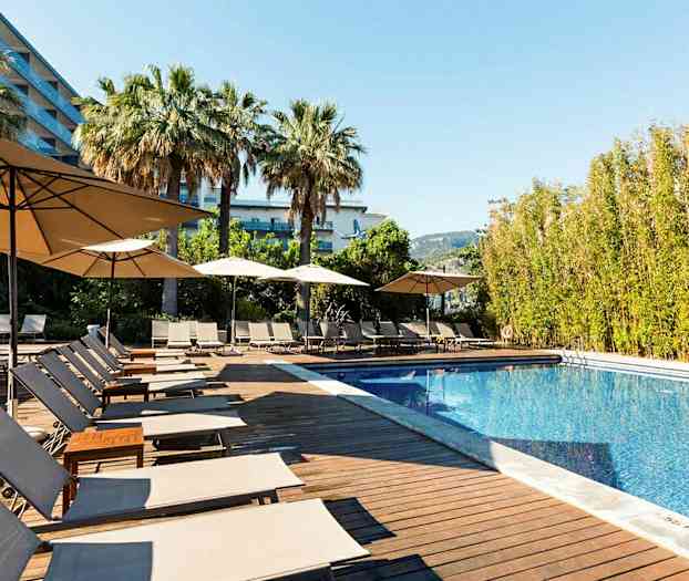 En utomhuspool med solsängar och parasoller omgiven av palmer och träd. (AI-genererad text)