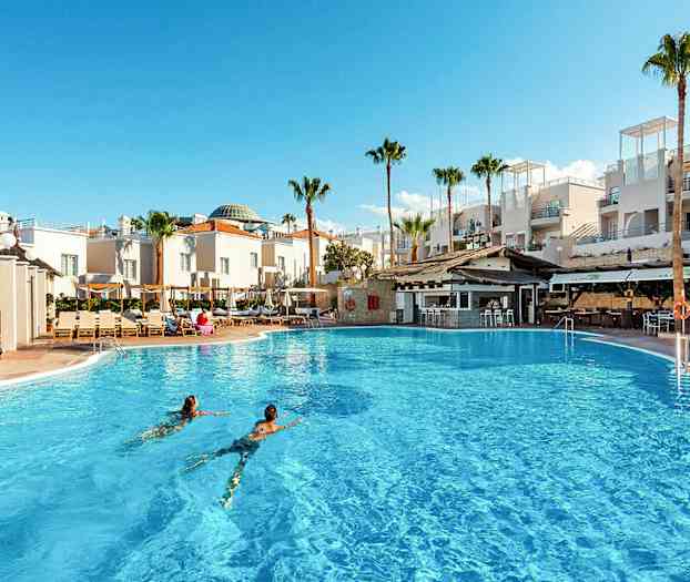 En stor utomhuspool framför vita byggnader och palmer. (AI-genererad text)