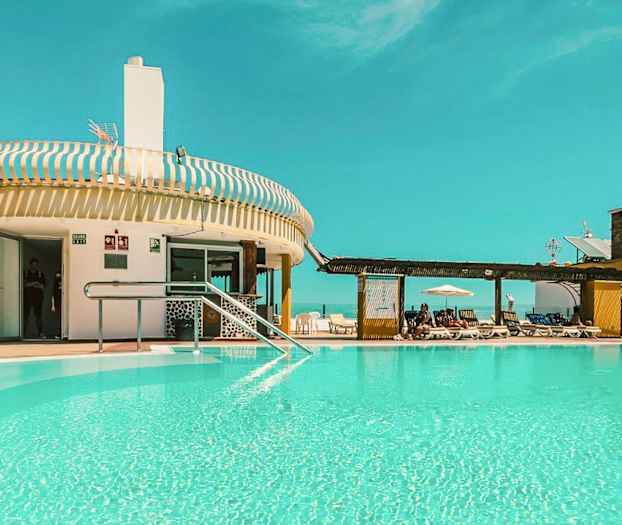 En utomhuspool vid en byggnad med solstolar och ett klart blått himmel. (AI-genererad text)