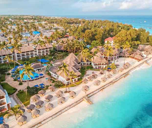 Luftvy som visar en strandnära resort med tropiska byggnader omgivna av palmer nära turkost vatten. (AI-genererad text)