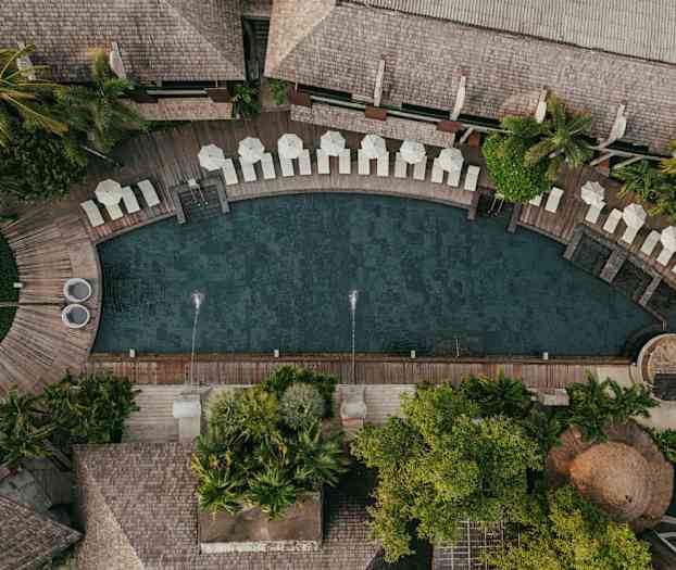 Flygfoto av en pool omgiven av solstolar, parasoller och lummig växtlighet. (AI-genererad text)