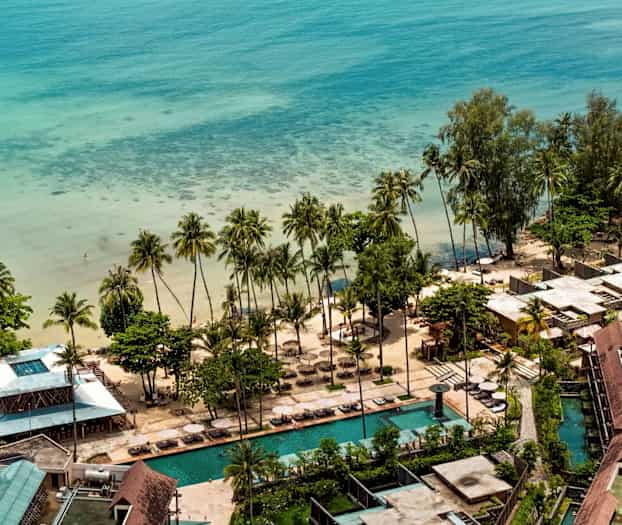 Flygbild över en strandresort nära havet med palmer, sandstrand och pooler. (AI-genererad text)