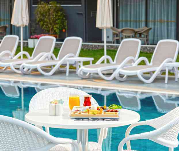 Ett bord med serverad mat och dryck intill en pool med solstolar i bakgrunden. (AI-genererad text)