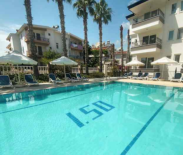 En utomhuspool omgiven av solstolar och parasoller med lägenhetsbyggnader i bakgrunden. (AI-genererad text)