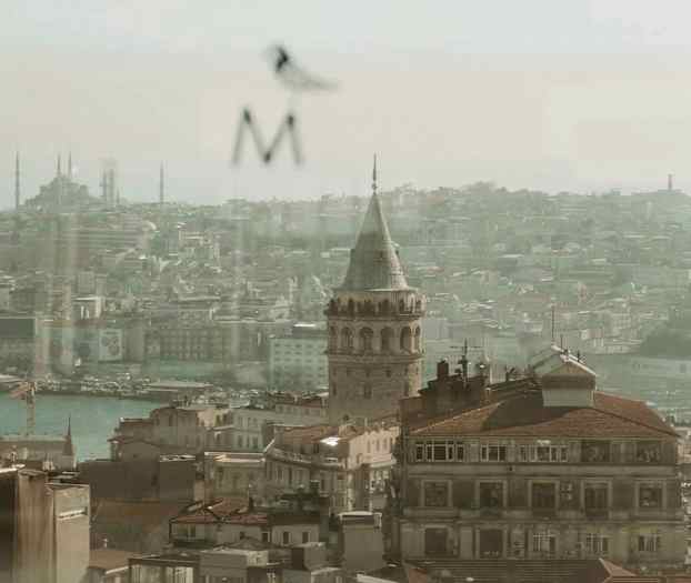 Utsikt över en stad med en historisk stenbyggnad toppad med ett torn, hustak och en flod i förgrunden. (AI-genererad text)