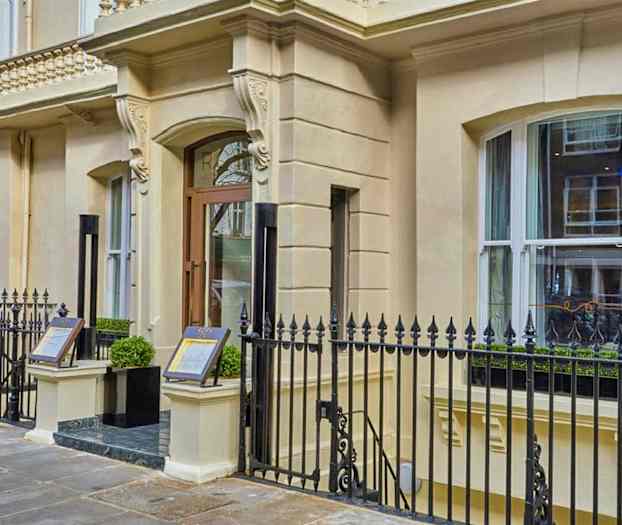 Ingång till en byggnad med dekorerad fasad och metallstaket. (AI-genererad text)