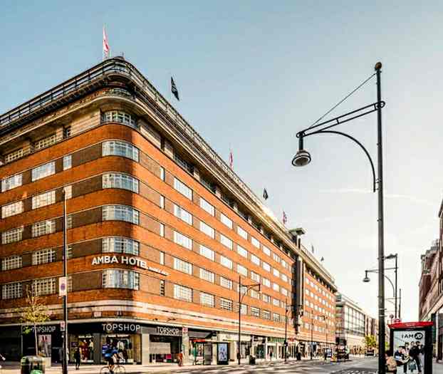 Ett stort tegelbyggnad med flaggor på toppen och butiker vid gatuplan. (AI-genererad text)