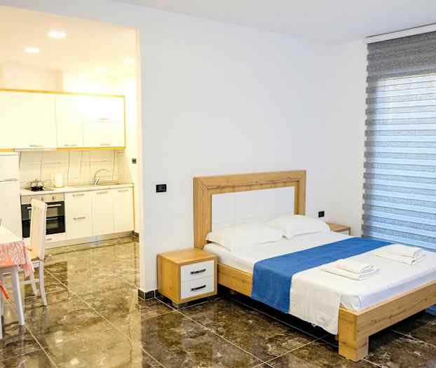 Ett sovrum med en dubbelsäng, bord med stolar samt en liten köksdel. (AI-genererad text)