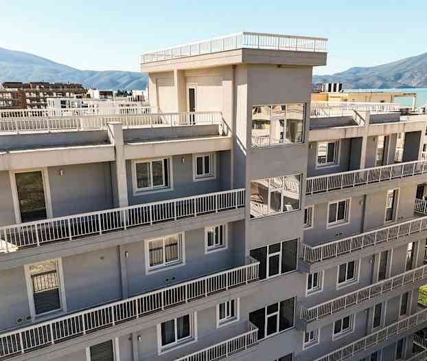 En modern byggnad med flera våningar och balkonger, omgiven av grönska och omgivande berg i bakgrunden. (AI-genererad text)