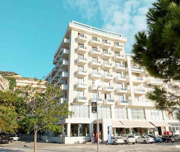 En bild av ett flervåningshotell med vita balkonger och träd i förgrunden. (AI-genererad text)