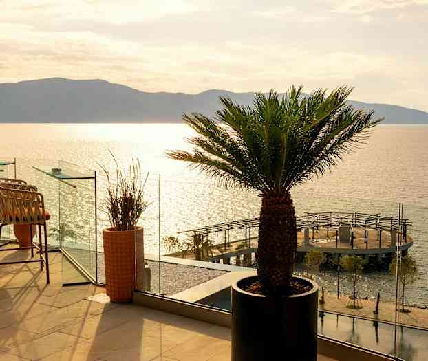 En terrass med stolar och palmer och utsikt över havet och en brygga. (AI-genererad text)