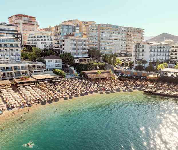 Hotell och parasoller vid en strand med klart vatten. (AI-genererad text)