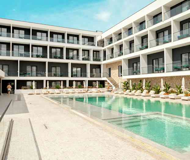 Hotellbyggnad med pool och solstolar i förgrunden. (AI-genererad text)