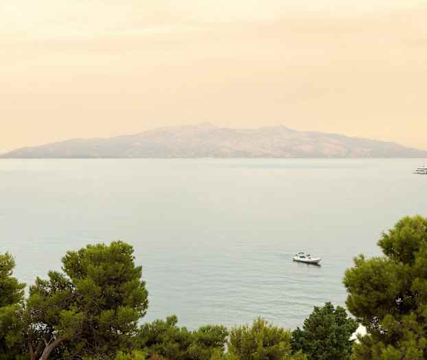 En avlägsen ö syns över havet med träd i förgrunden och två båtar i vattnet. (AI-genererad text)