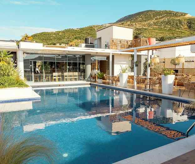 En modern byggnad med glasfasad bredvid en utomhuspool, omgivet av grön vegetation. (AI-genererad text)