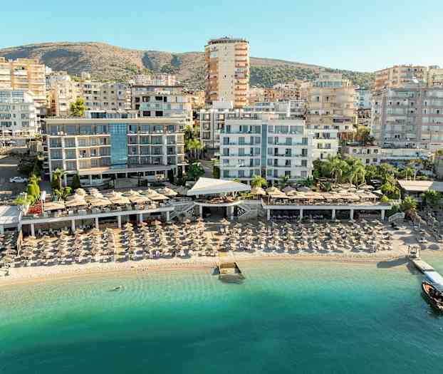 Vy över strand med solstolar och hotellbyggnader i bakgrunden. (AI-genererad text)