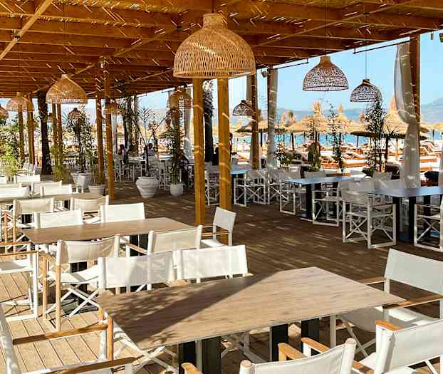 Bild på en utomhusservering med träbord och vita stolar under en träpergola. (AI-genererad text)