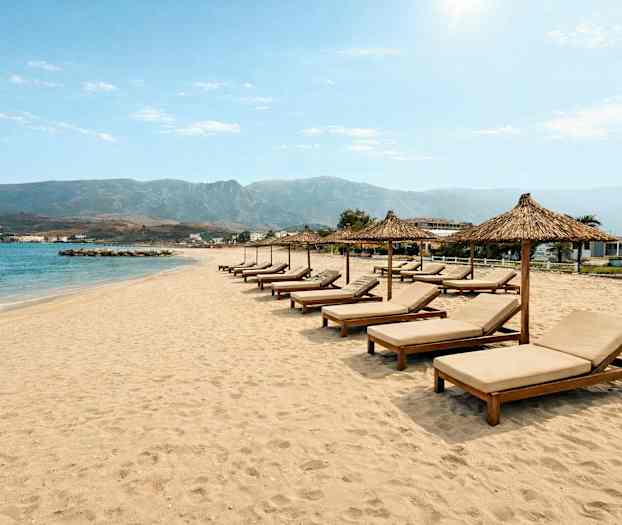 En sandstrand med solstolar och parasoller på rad framför havet. (AI-genererad text)