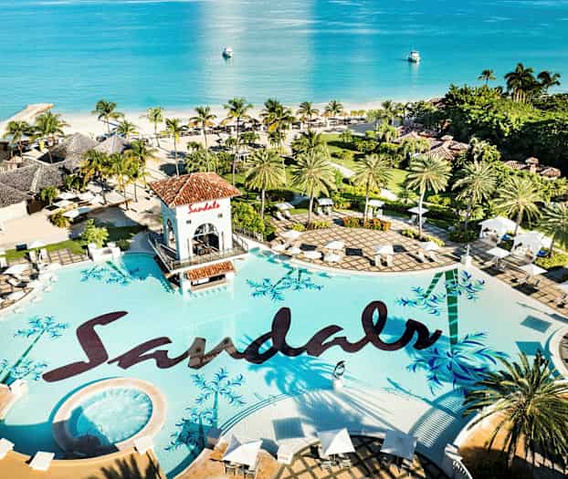 En stor pool med texten 'Sandals', omgiven av palmer och parasoller, med utsikt över havet. (AI-genererad text)