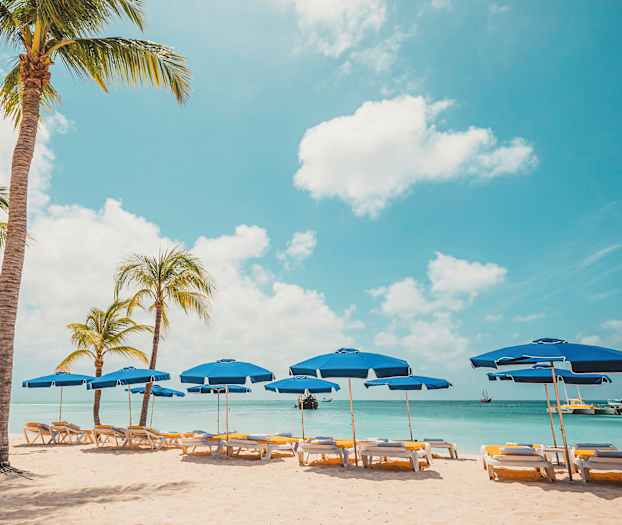 Strand med palmer och blå parasoller vid vattnet. (AI-genererad text)