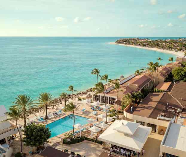 Utsikt över kustområde med turkost hav och resort med pool och palmträd. (AI-genererad text)