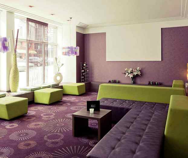 Ett ljust rum med lila väggar och golvmatta, gröna sittplatser och stora fönster. (AI-genererad text)