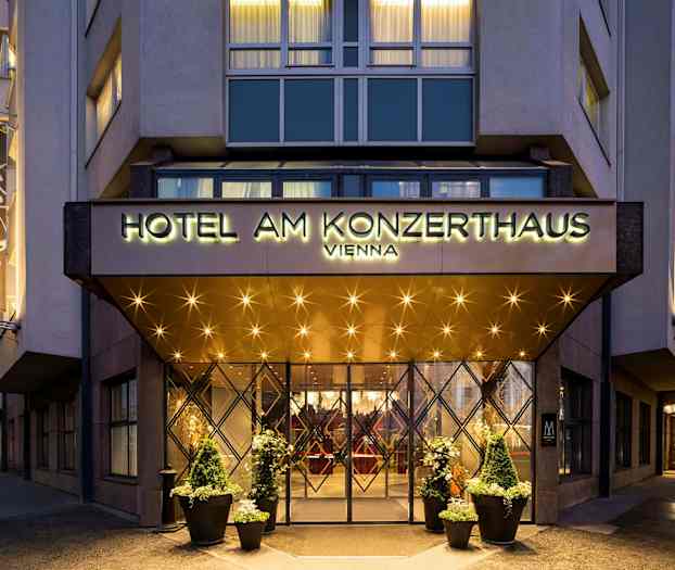 Entrén till ett hotell med en skylt som lyder "Hotel am Konzerthaus Vienna". Belysning och dekorationer syns runt ingången och på fasaden. (AI-genererad text)