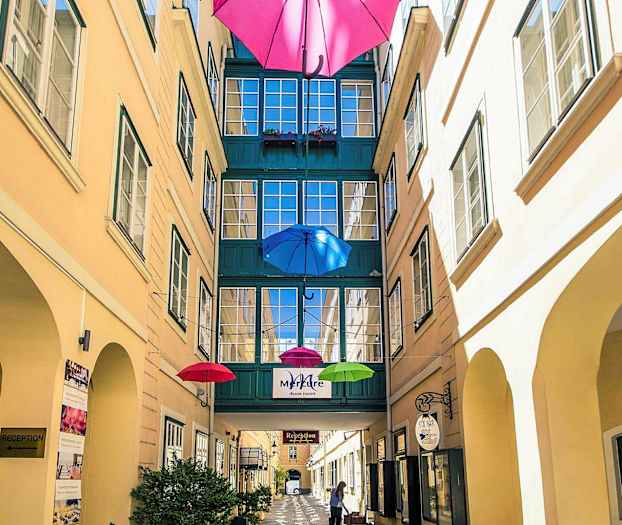 En smal innergård med färgglada paraplyer hängande ovanför och en passage mellan byggnader. (AI-genererad text)