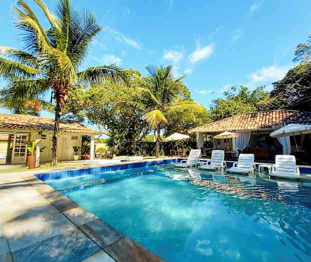 En swimmingpool omgiven av solstolar, parasoller och palmer vid en byggnad i soligt väder. (AI-genererad text)