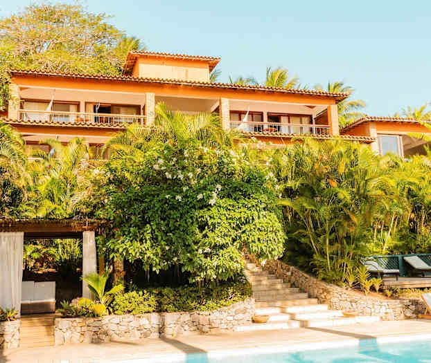 Bild på en byggnad med flera våningar omgiven av grönskande växter, med en pool i förgrunden. (AI-genererad text)